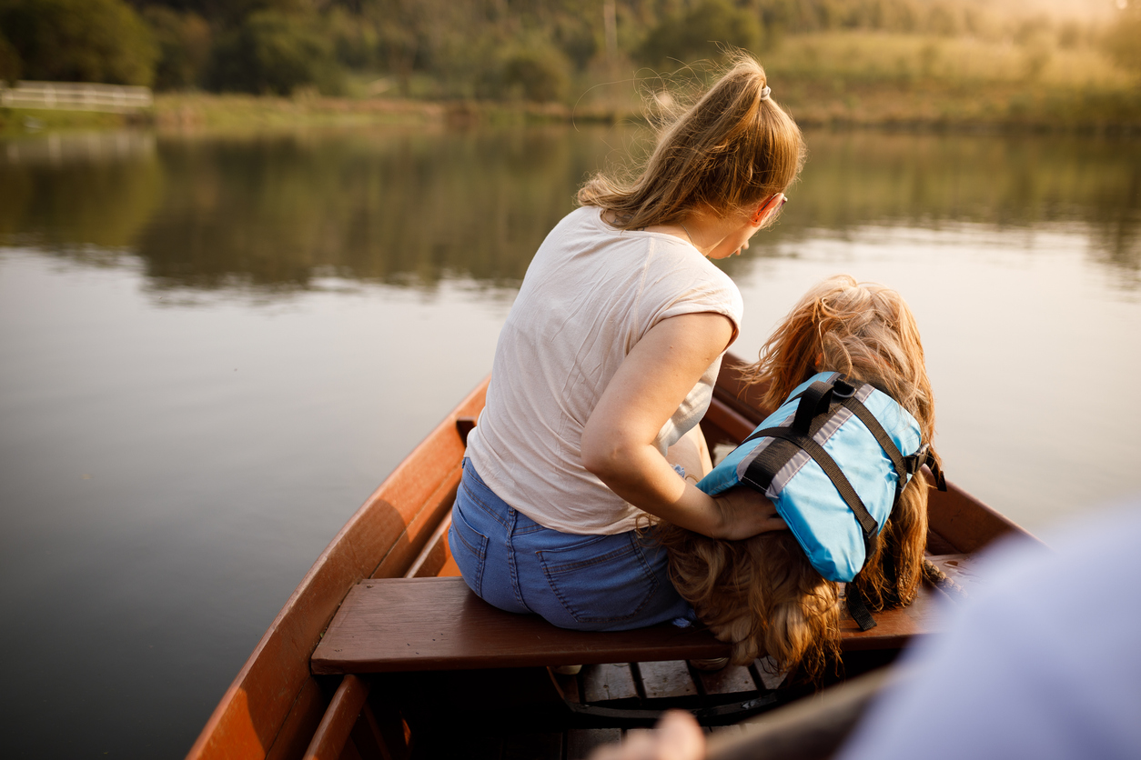 Frau und Hund mit Schwimmweste sitzen in einem Boot.